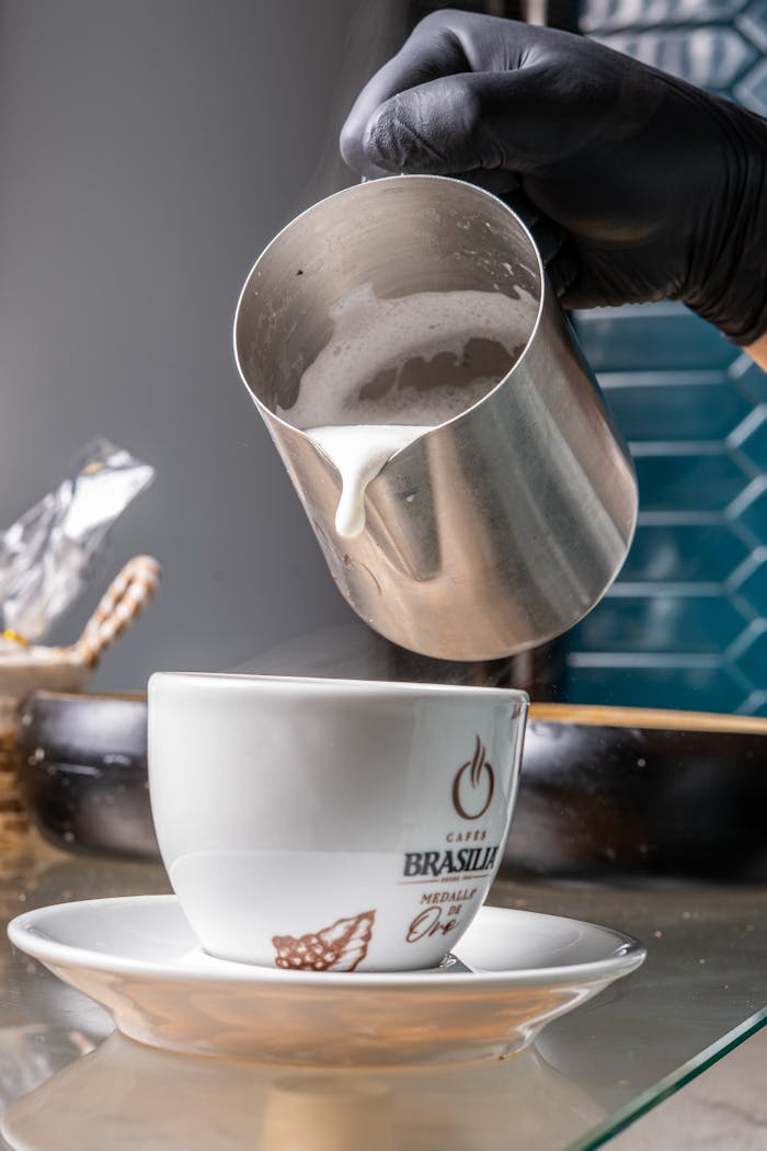 Close-up of a barista pouring steamed milk into a coffee cup indoors.