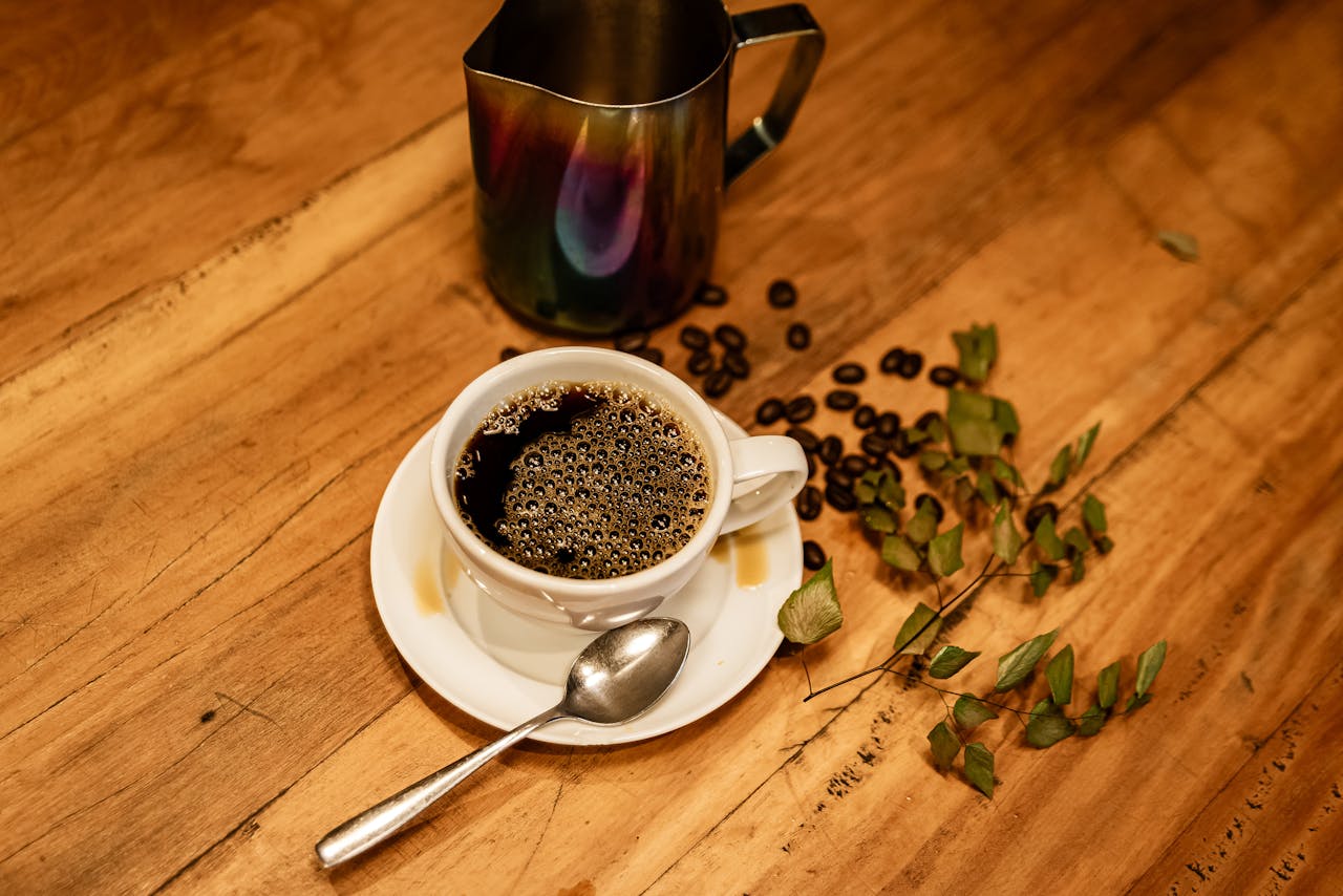 services-02 Elegant coffee scene with a coffee cup, roasted beans, and a metal jug on a wooden table.